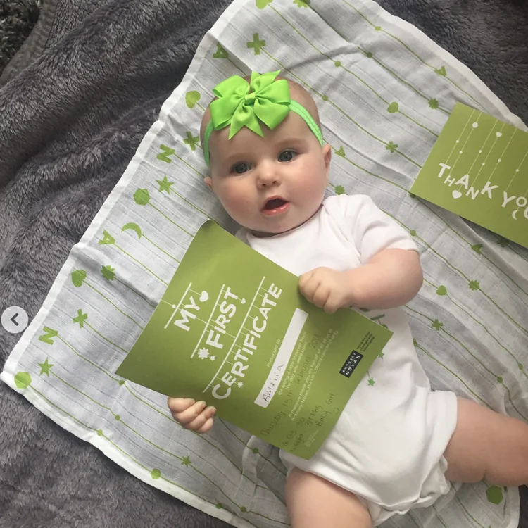 Baby with a green bow lying on the muslin with the &lsquo;My first certificate&rsquo;