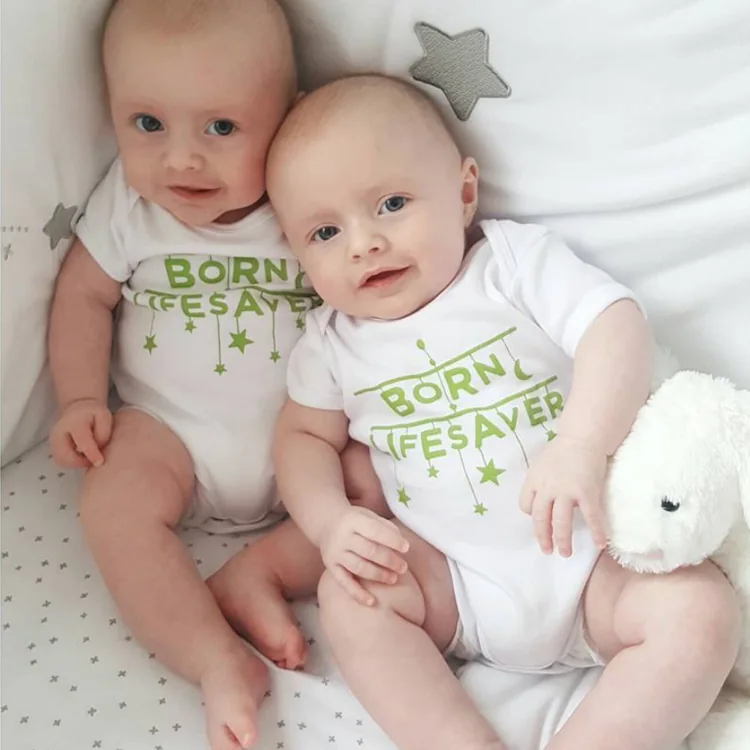 Twin babies side by side, one in a &lsquo;Born lifesaver&rsquo; babygrow