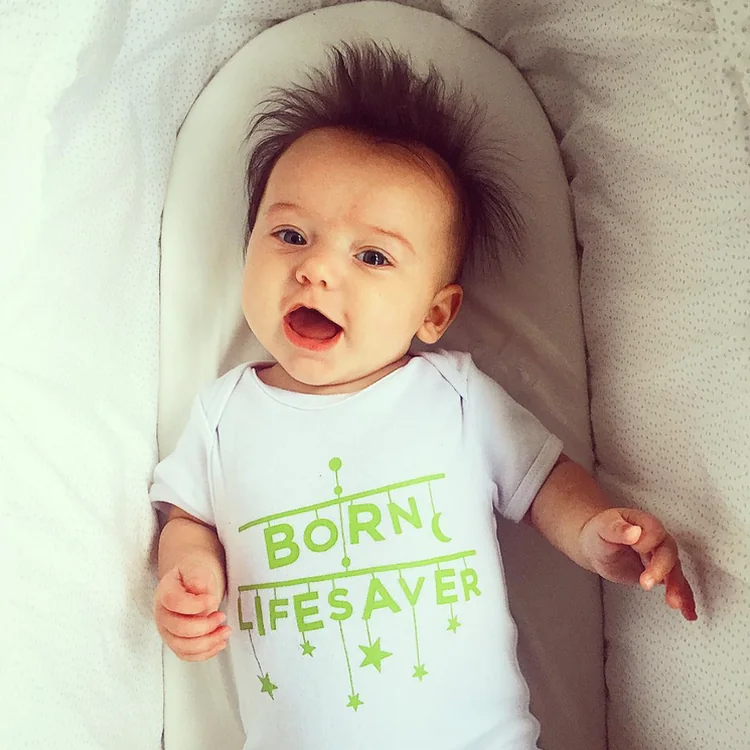 Smiling baby with spiky dark hair in a &lsquo;Born lifesaver&rsquo; babygrow