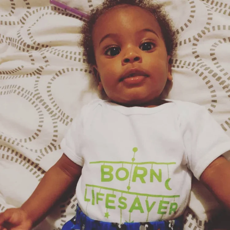 Baby in a &lsquo;Born lifesaver&rsquo; babygrow looking up at the camera