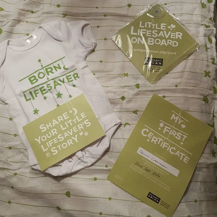 Flat lay of the bundle: babygrow, car sign, postcard and certificate on the muslin