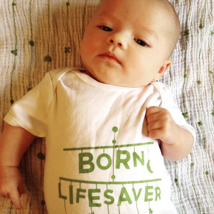 Baby in a &lsquo;Born lifesaver&rsquo; babygrow looking at the camera