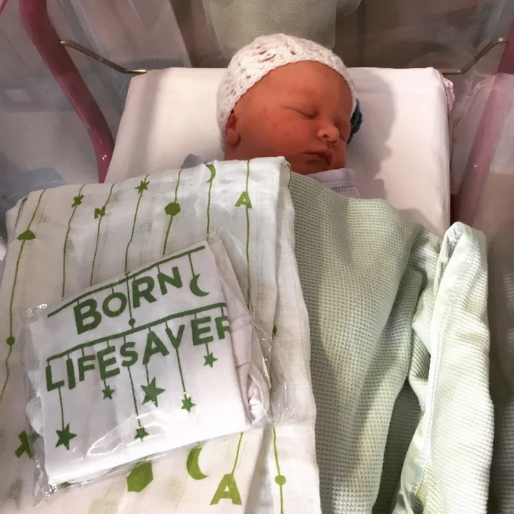Newborn in a cot with a folded &lsquo;Born lifesaver&rsquo; babygrow