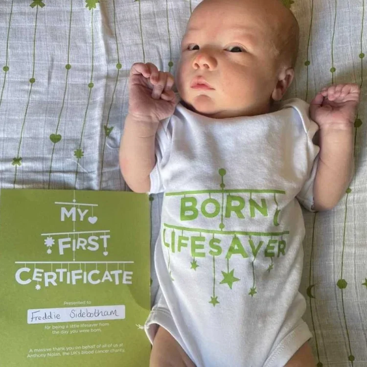 Newborn in a &lsquo;Born lifesaver&rsquo; babygrow on the muslin, with a named &lsquo;My first certificate&rsquo;