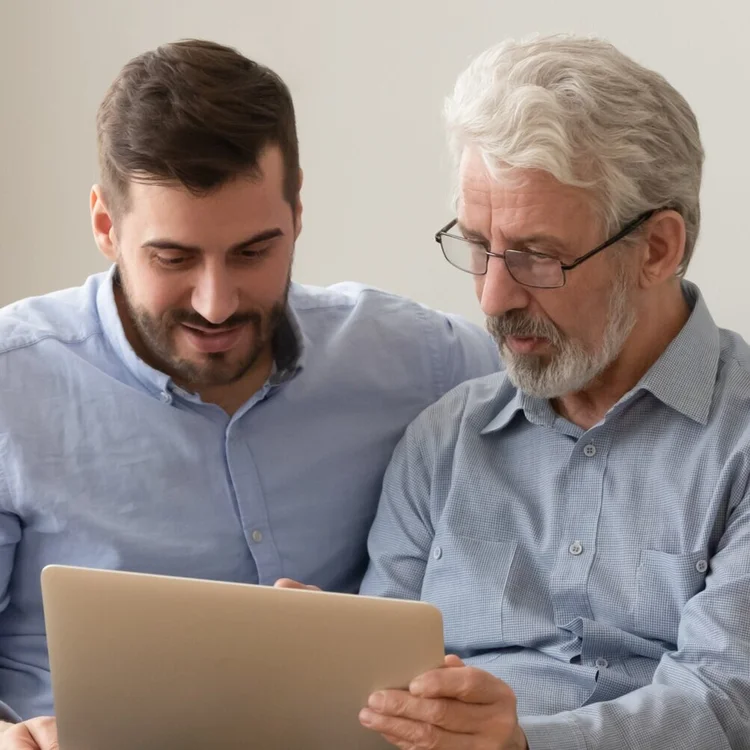 Persona photo: a younger man helping an older man use a laptop, representing a family member