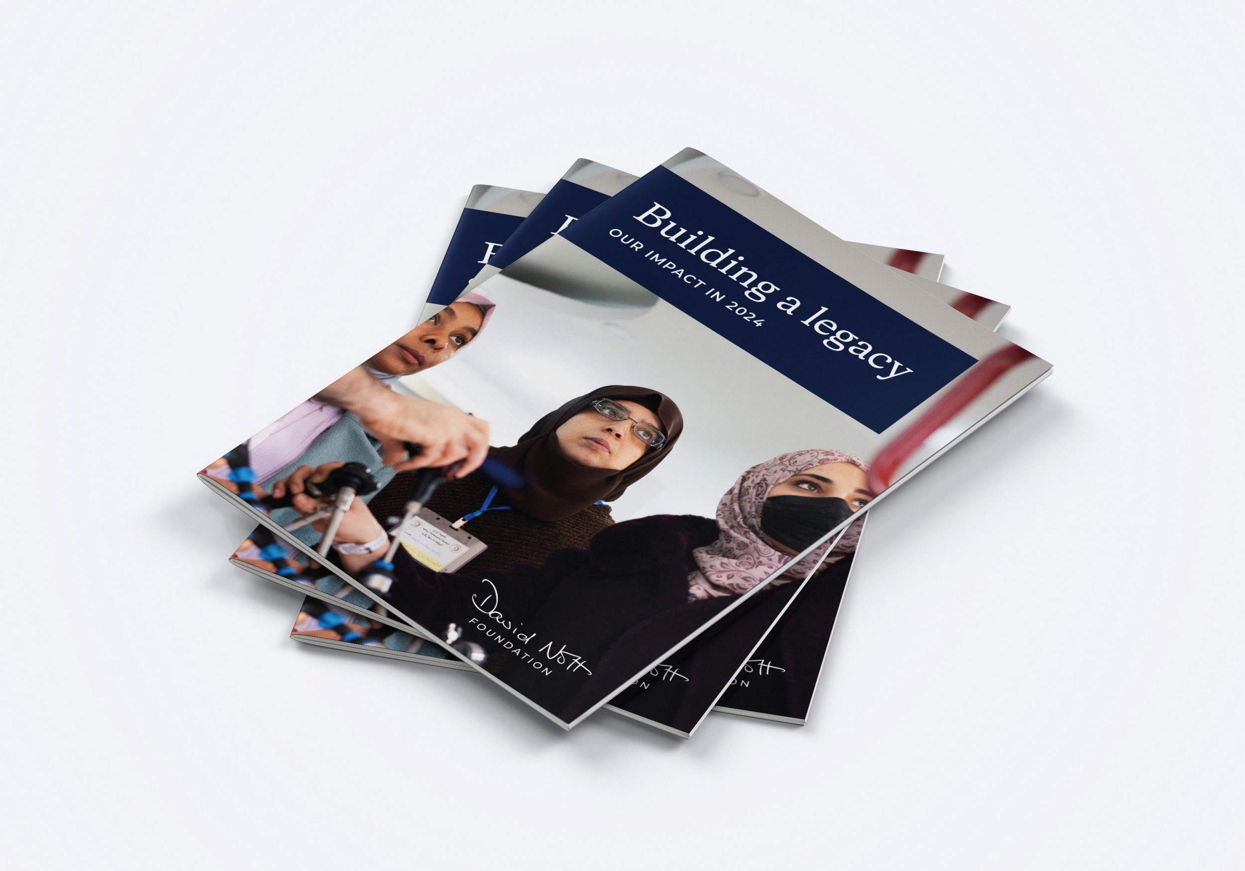 A stack of &lsquo;Building a legacy: our impact in 2024&rsquo; reports, with a photo of women in hijabs at a surgical training session on the cover
