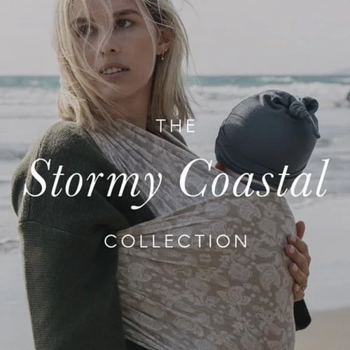 A woman carrying a baby in a sling on a beach, with &lsquo;The Stormy Coastal Collection&rsquo; in a script typeface