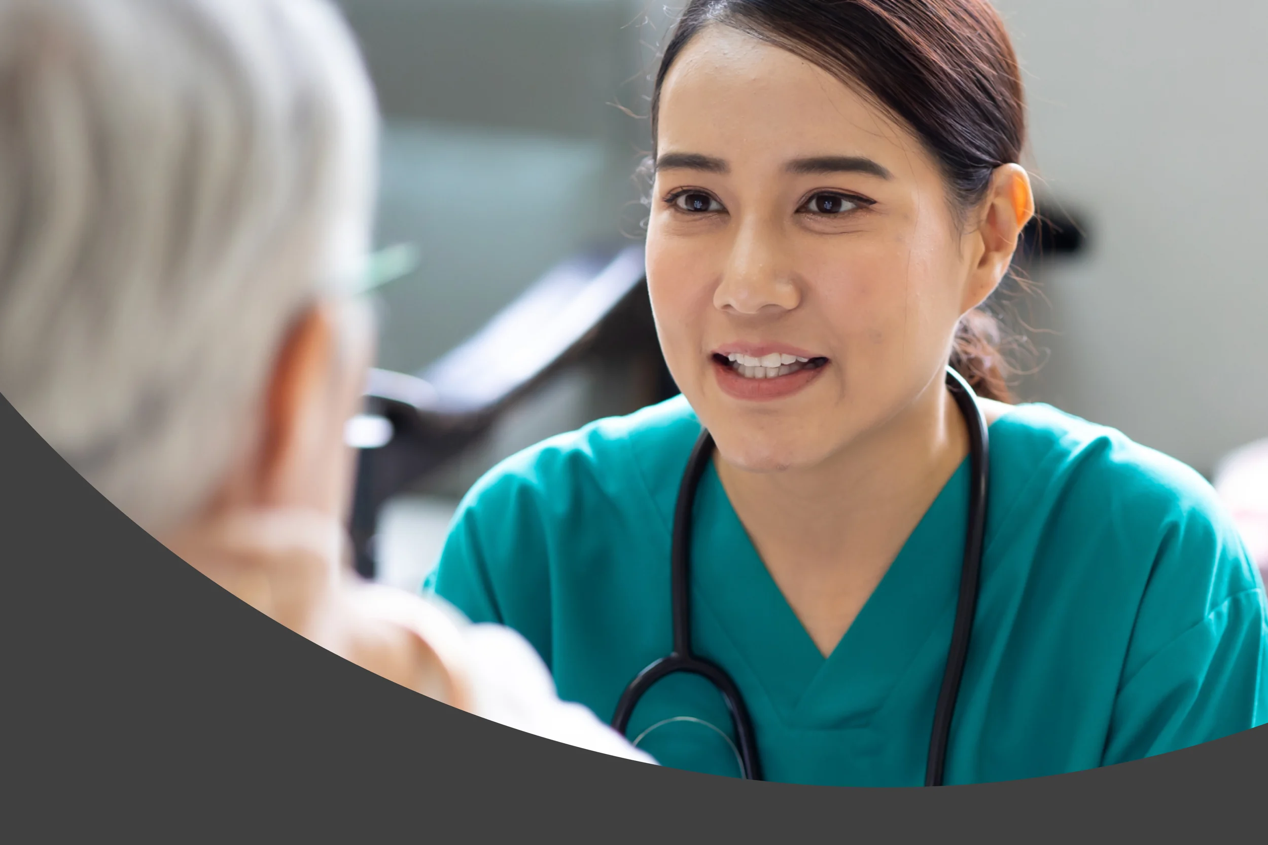 Photographic style: a smiling nurse in teal scrubs talking with a patient, with a curved dark grey shape along the bottom